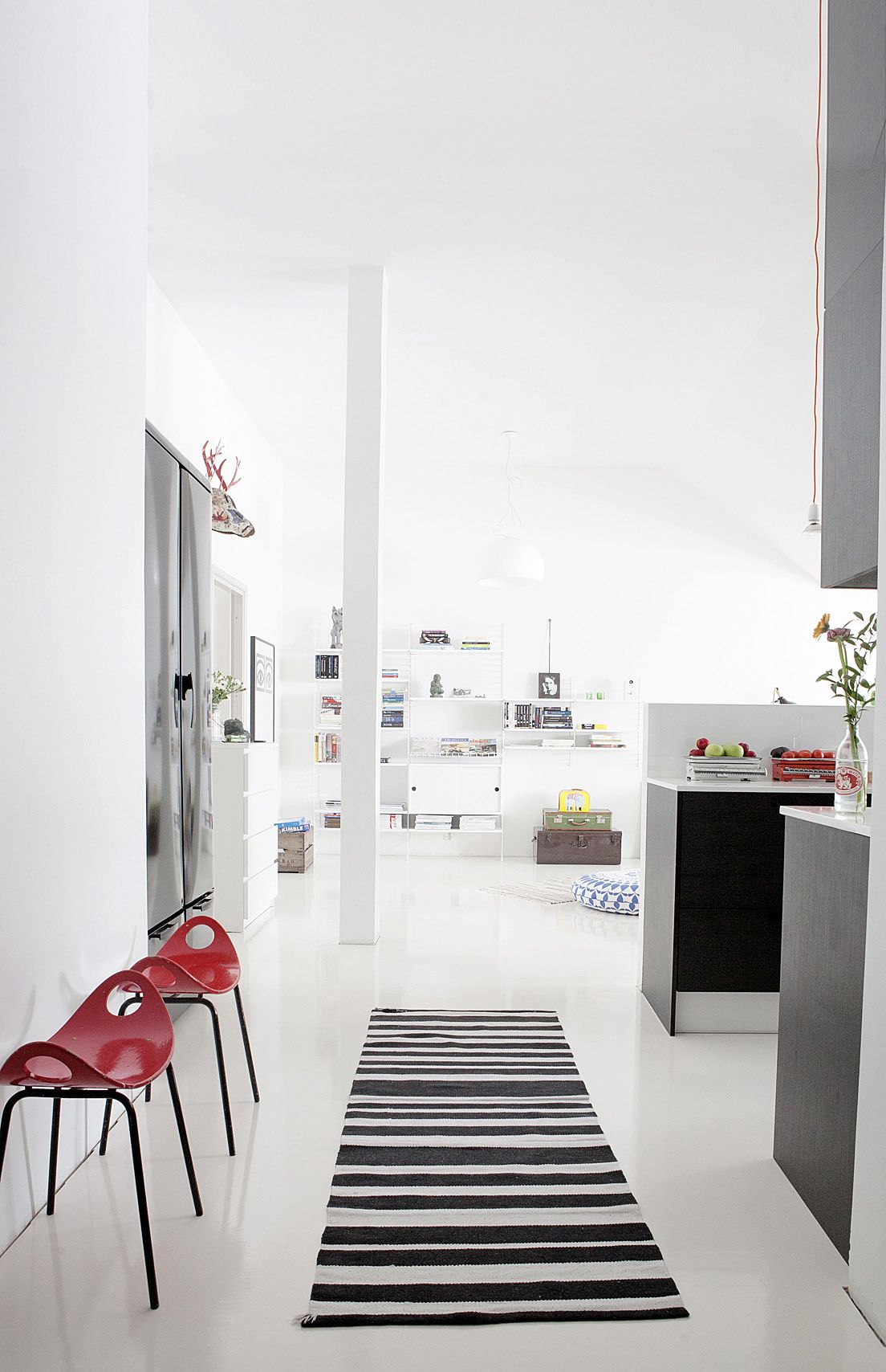 Eteisen päässä avautuu näyttävä oleskelutila kirjahyllyineen. Vanhat punaiset tuolit ovat perintöä Kaikun ukilta. Raitamatto, Hemtex.