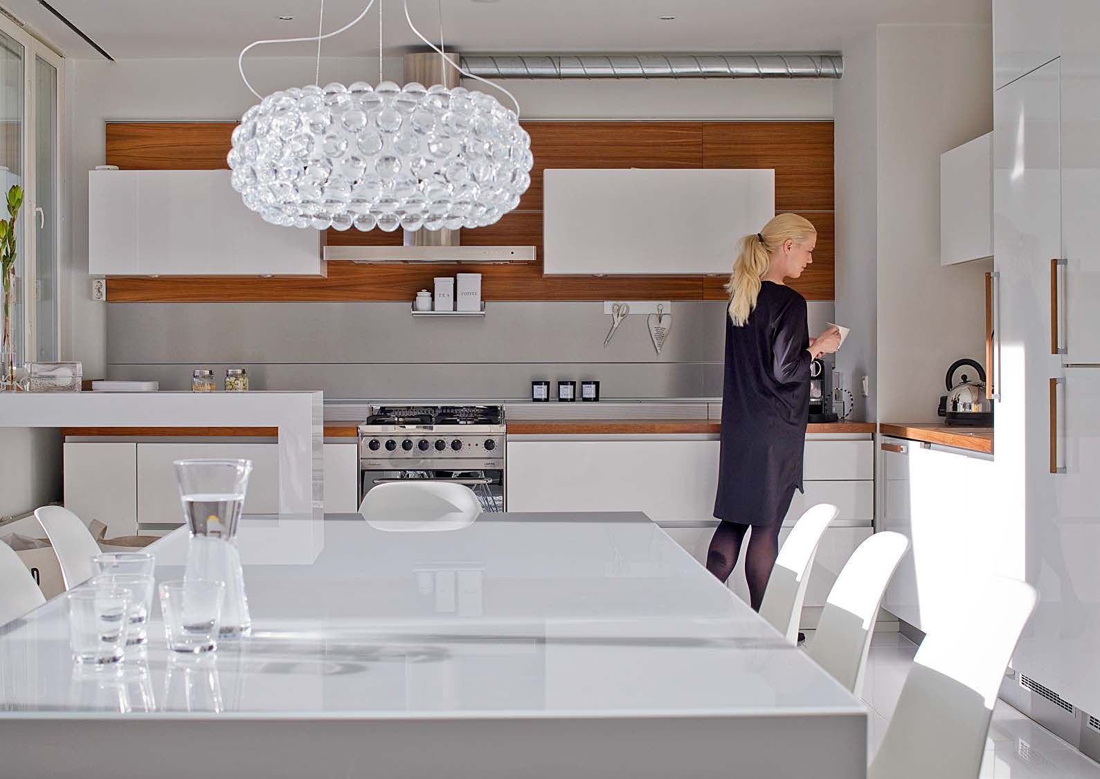 Keittiössä vanha, massiivinen saareke korvattiin kevyellä tasolla. Mikroaaltouuni ja viinikaappi kätkettiin kaapistoon. Ruokapöydän valkoista pintaa suojaa lasi.