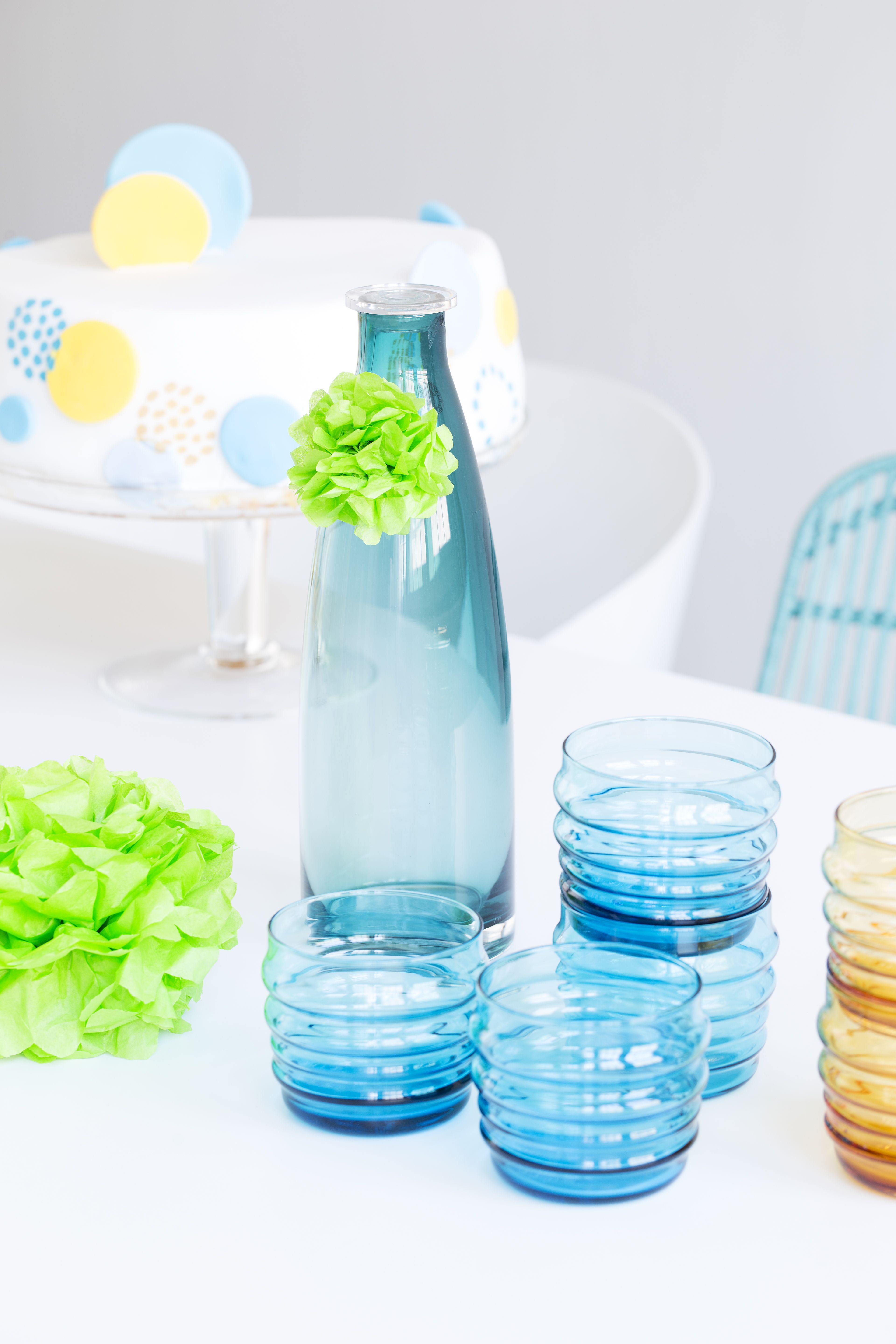 Paperipallot somistavat pöydässä pullonkauloja ja lasinjalkoja. Pieni pompom syntyy 8 x 11 sentin kokoisista silkkipaperipaloista, joita on pinossa viisi kappaletta. Taittele arkkipino sentin levyisille vekeille, solmi keskeltä ja avaa kuohkeaksi palloksi.