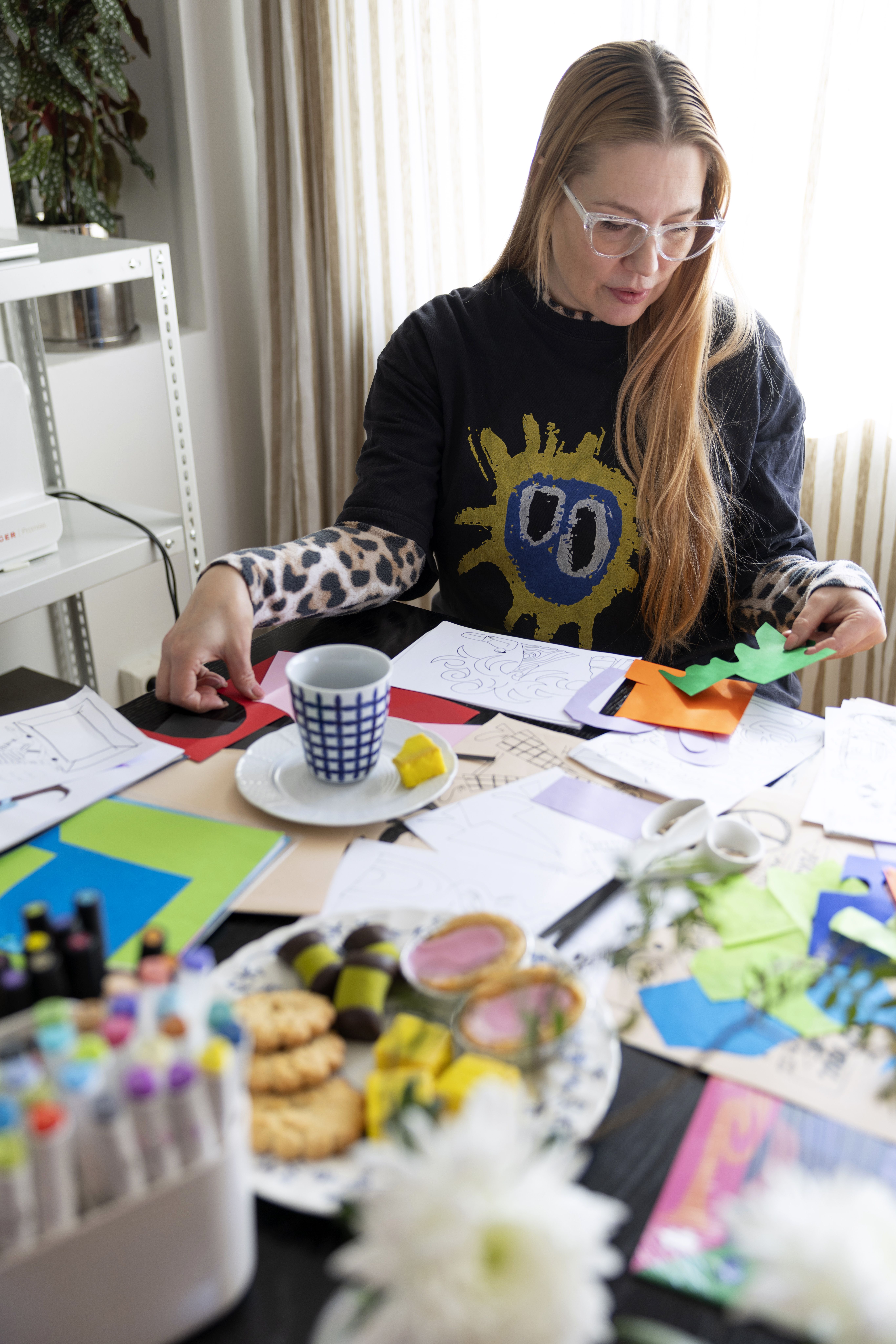 Mander tekee kuvituksia aiempaa enemmän käsin, sillä tietokoneen ääressä istuminen kyllästyttää. Pehmeä leopardimekko ja sen päälle puettu printtipaita ovat mukava työasu. ”Vanhenemisessa on ihanaa se, että osaa tehdä itselleen mukavat olot.”