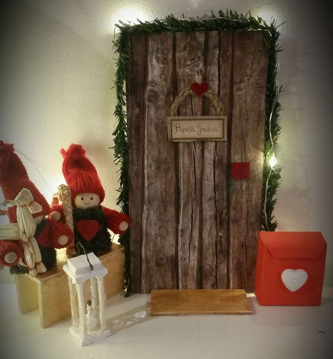 "Meidän tontun ovi syntyi osittain valmispaketista. Kranssi on punottu itse ja postilaatikko tehty karkkilaatikosta. Lyhtykin&nbsp;on värkätty käsin tulitikuista, lasit liivatelehdestä. Oven ympärille liimattiin&nbsp;valmista askarteluhavupunosta. Led-valot koristavat ympärillä." Tuula Ratilainen