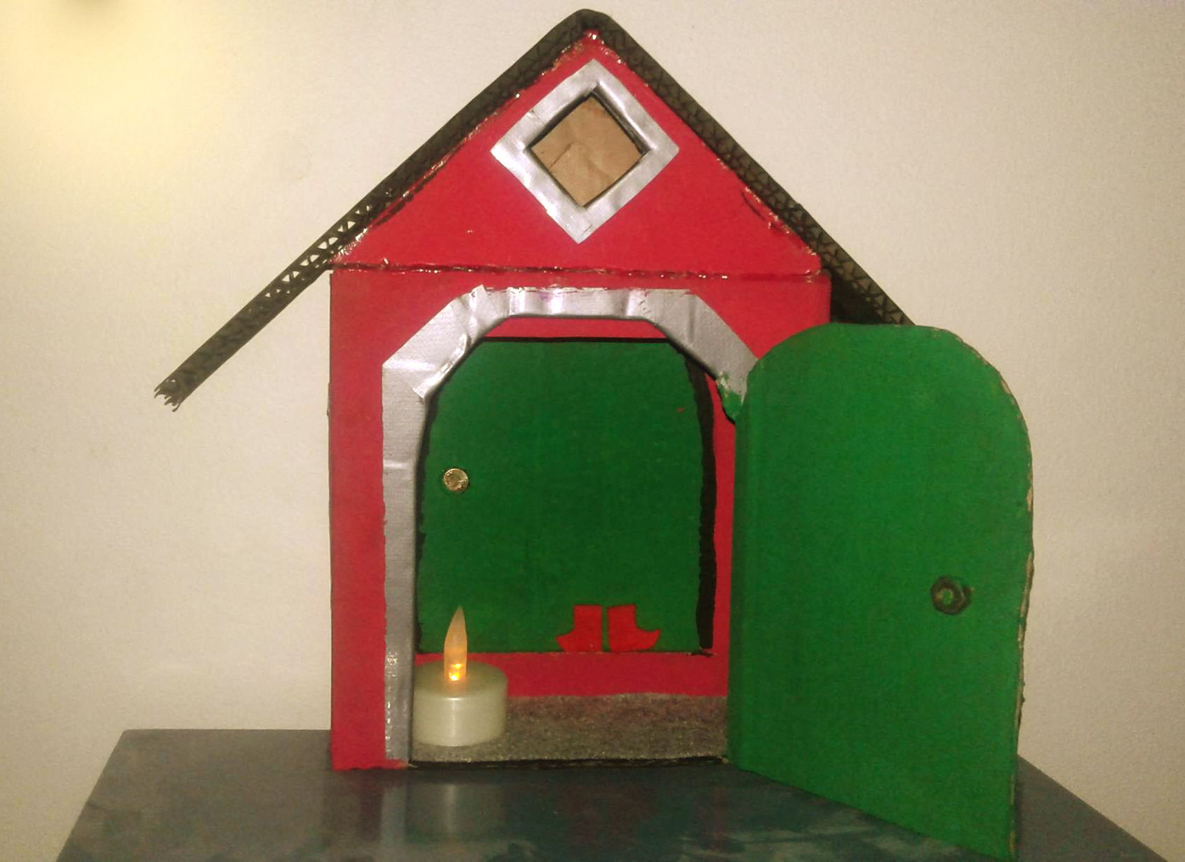 "Itse värkätty töissä muksulta salaa. Pahvilaatikko oli idean lähde. Avattava ovi ja näin ollen "ulkoporstua", jonka sisään mahtuu ledikynttilä. Maalattu akryylimaalein. Huopamatto ja tossut sisäoven kynnyksellä. Tämän paikka on meillä eteisessä naulakon vieressä erään rompelaatikon päällä. Muksu jättää tontulle pipareita ja&nbsp;namuja,&nbsp;ja tonttu jättää pieniä kulkusia." Mustikka Nevalainen