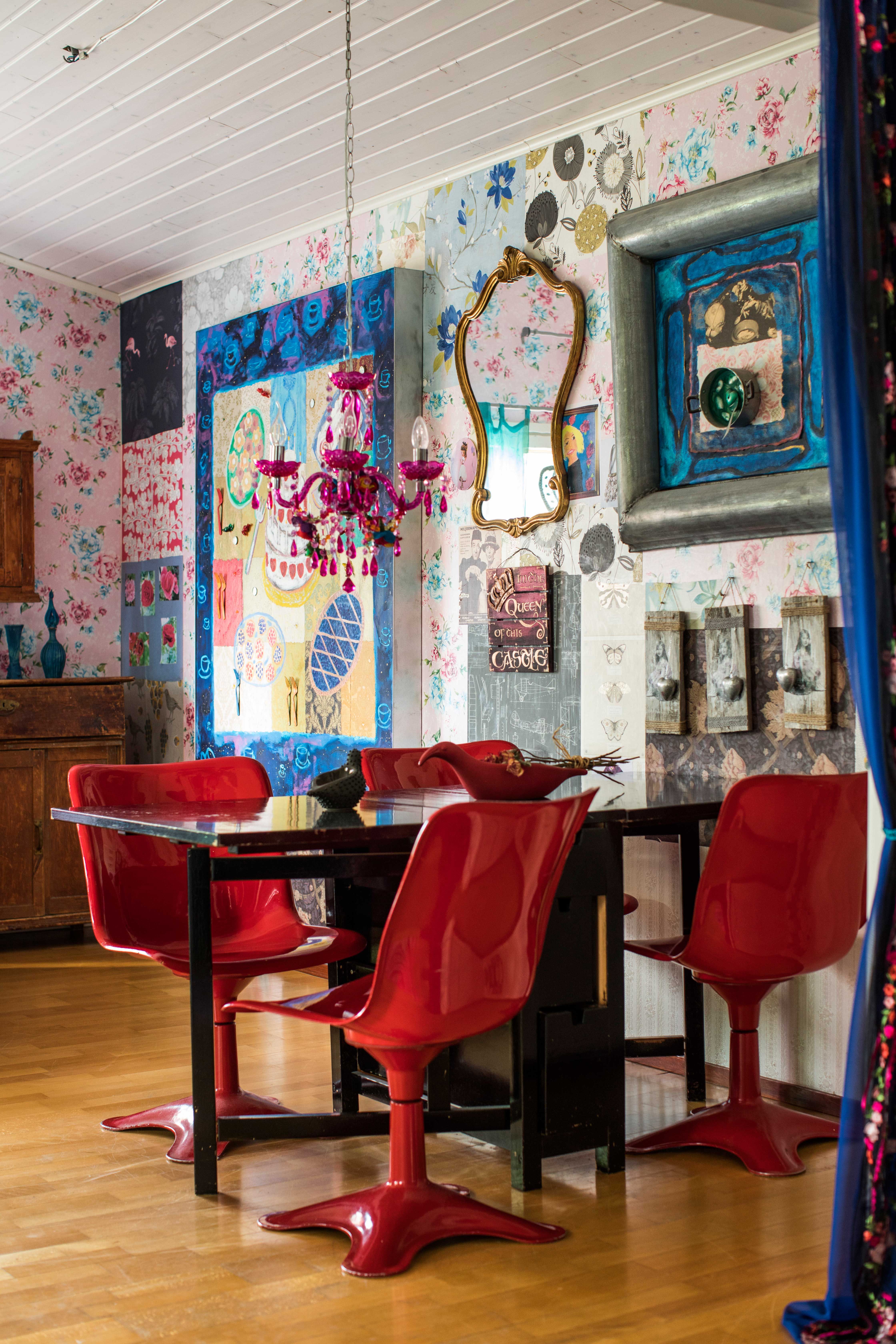 Olohuoneen seinä on koristeltu tapetinpaloilla ja tauluilla. Punaiset muovituolit tuovat tuulahduksen 1970-luvulta. 