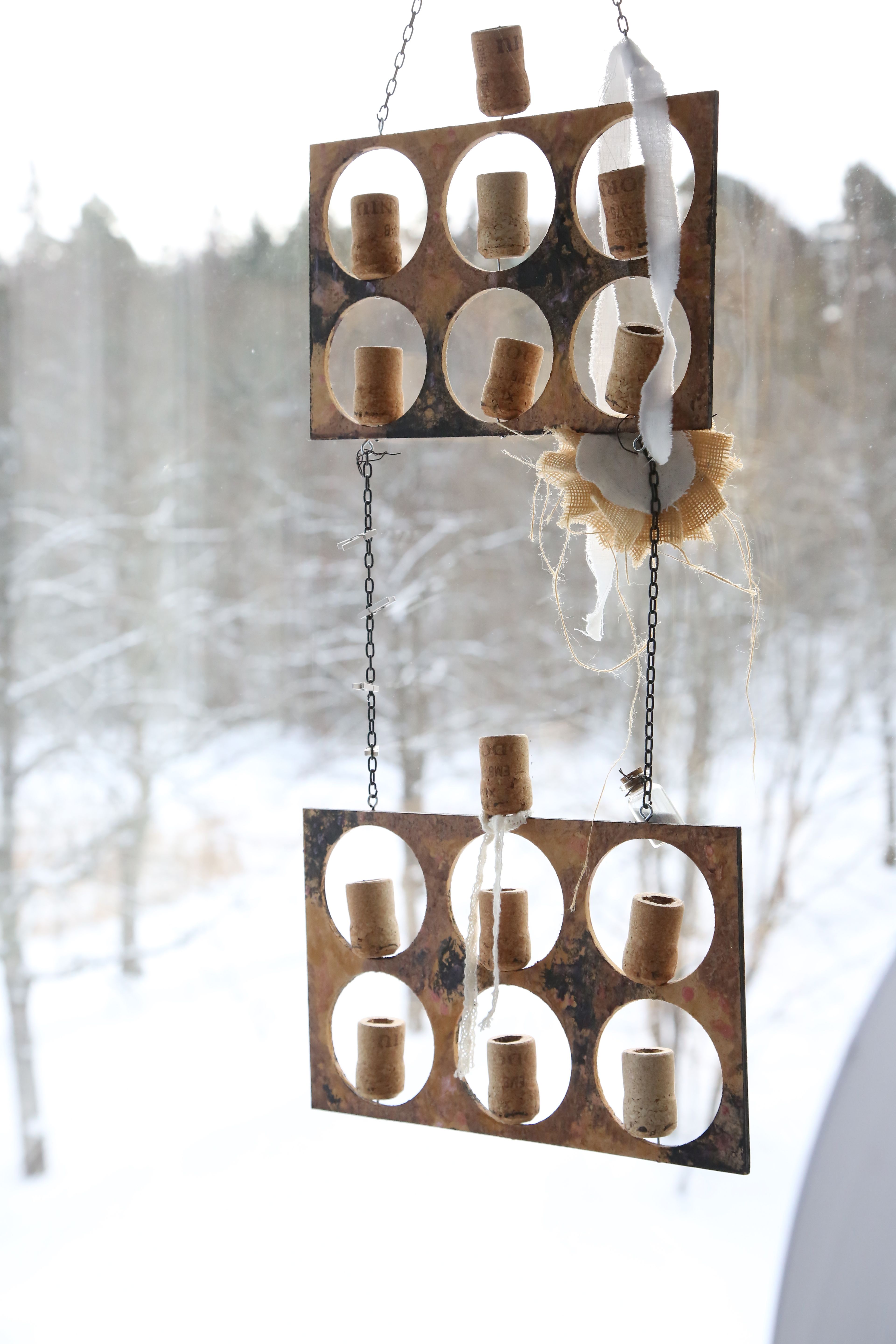 Uniikissa amppelissa on kaiverrettuja samppanjakorkkeja, joihin mahtuu vähän multaa ja pieni pistokas. Kesällä korkit kukkivat.